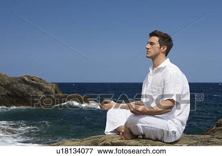 Stock Photo - A man meditating by the sea. Fotosearch