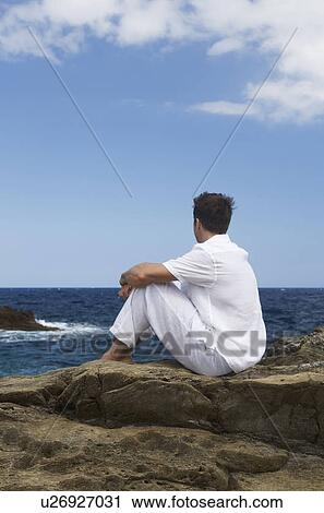 Stock Image - A man sitting by the sea. Fotosearch