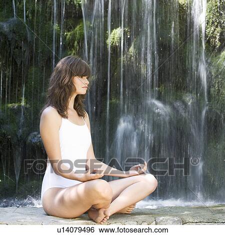 Stock Photograph - A woman meditating by a waterfall. Fotosearch