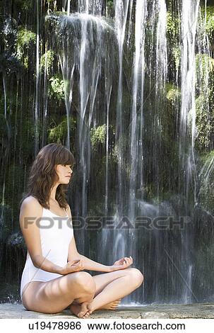 Stock Photograph - A woman meditating by a waterfall. Fotosearch