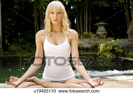 Stock Image - Beauty portrait of a woman in the lotus position doing yoga in a tropical setting.. Fotosearch