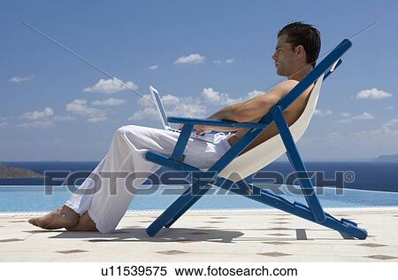 A man sitting on a deck chair using a laptop View Large Photo Image Stock Photography - A man sitting on a deck chair using a laptop. Fotosearch