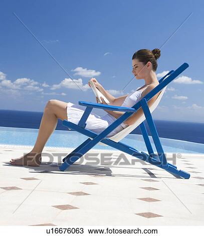 A woman sitting on a deck chair reading a book View Large Photo Image Stock Image - A woman sitting on a deck chair reading a book. Fotosearch