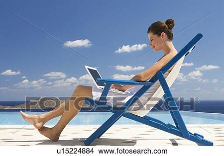 Picture - A woman sitting on a deck chair using a laptop. Fotosearch