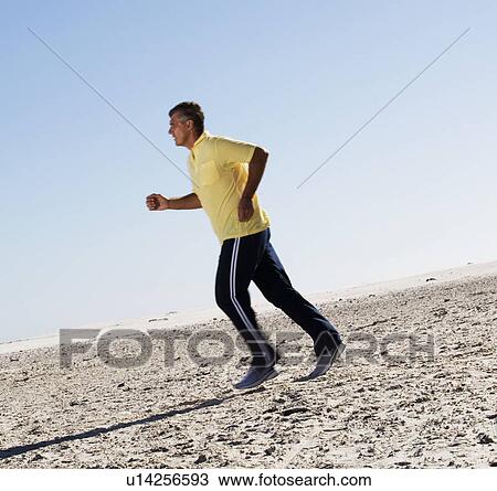 Stock Image - A man jogging on a beach. Fotosearch