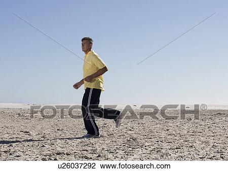 Stock Image - A man jogging on a beach. Fotosearch