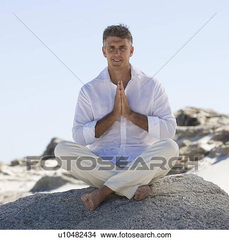 Picture - A man sitting on rocks performing yoga. Fotosearch