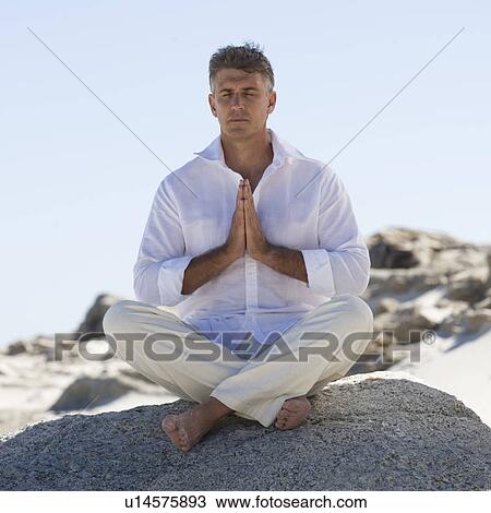 Stock Image - A man sitting on rocks performing yoga. Fotosearch