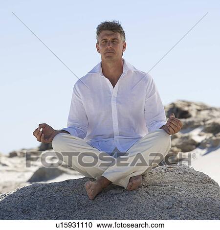 Stock Image - A man sitting on rocks performing yoga. Fotosearch