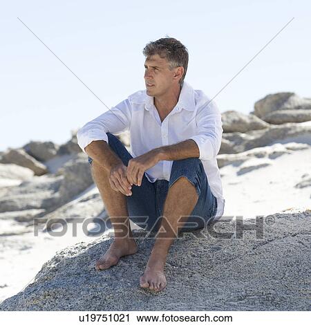 Stock Image - A man sitting on rocks. Fotosearch