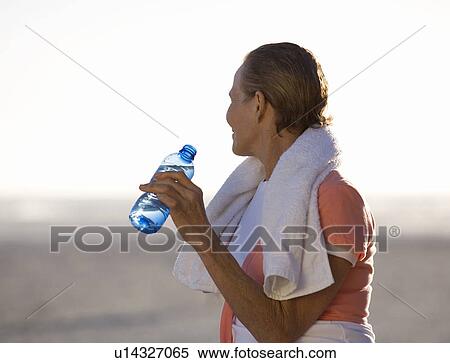 Stock Photography - A mature woman drinking a bottle of water. Fotosearch