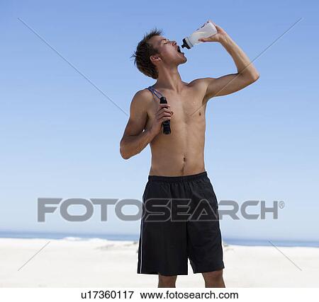A young man drinking from a water bottle after exercising View Large Photo Image Stock Photo - A young man drinking from a water bottle after exercising. Fotosearch