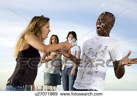 Stock Photo - Young woman throwing a drink over a man at party. Fotosearch