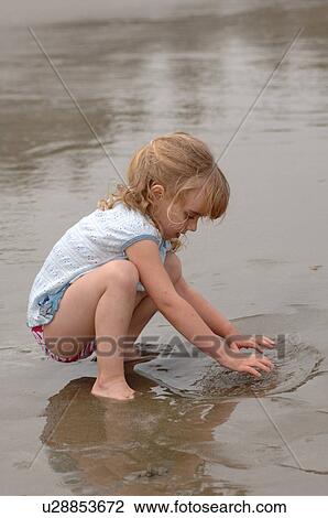 Stock Image - 3 Year old playing in water on beach. Fotosearch
