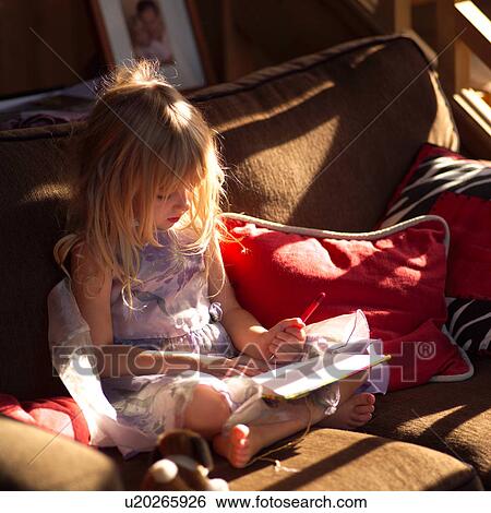 Stock Photograph - 5 year old sitting on a sofa and writing in a book. Fotosearch