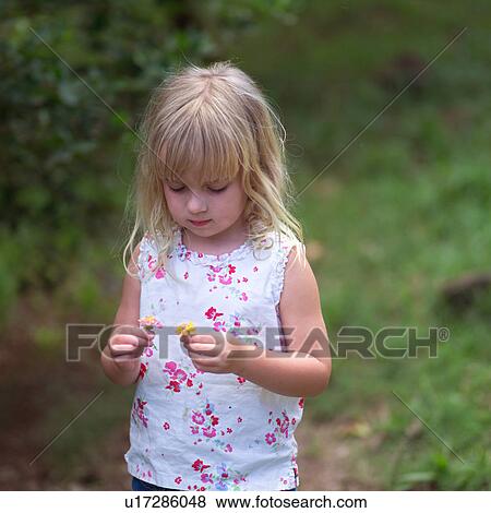 Stock Photo - Blond Girl looking at a Flower. Fotosearch