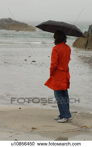 Stock Image - Ireland - woman on beach holding umbrella. Fotosearch