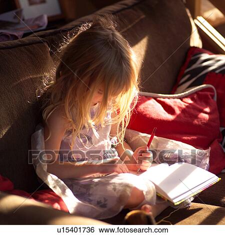 Stock Photograph - 5 year old sitting on a sofa and writing in a book. Fotosearch