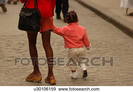 A woman holding her child walking on a street View Large Photo Image Stock Photo - A woman holding her child walking on a street. Fotosearch