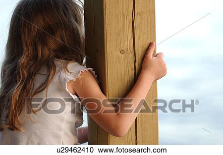 Stock Image - Young girl holding on to a wooden post. Fotosearch