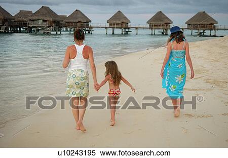 Stock Photography - A young girl (6-8) walking with two young women on a beach. Fotosearch