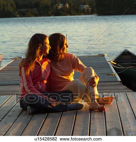 Mother and daughter sitting on dock at sunset View Large Photo Image Stock Image - Mother and daughter sitting on dock at sunset. Fotosearch