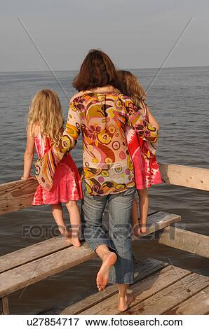 Stock Photo - Rear view of mother and daughters looking at the water. Fotosearch
