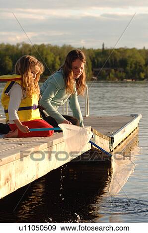 Stock Photo - Two girls kneeling at edge of dock. Fotosearch