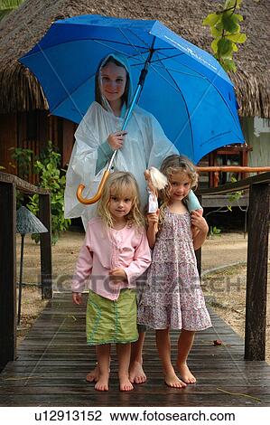 Stock Image - A young mother holding an umbrella standing with her two young daughters. Fotosearch