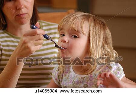 Mother feeding a young girl with a fork View Large Photo Image Picture - Mother feeding a young girl with a fork. Fotosearch