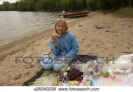 Stock Photo - Portrait of a young girl sitting on a beach holding a sandwich. Fotosearch