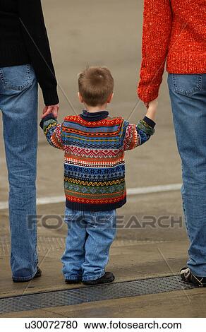 Stock Image - Rear view of two people holding a child's hands. Fotosearch