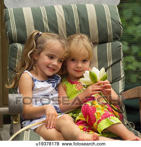Two young girls sitting in a chair holding a lotus View Large Photo Image Stock Photo - Two young girls sitting in a chair holding a lotus. Fotosearch