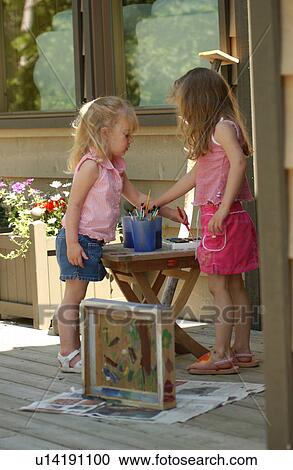 Stock Image - Two young girls standing and painting. Fotosearch