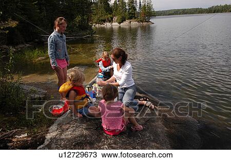 Stock Image - Young women with four young girls sitting on a rock. Fotosearch