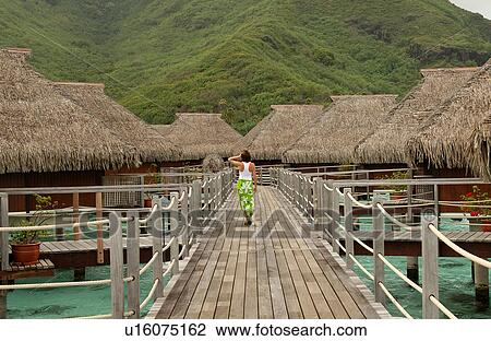 Stock Image - A young woman walking on a pier, Moorea, Tahiti, French Polynesia, South Pacific. Fotosearch