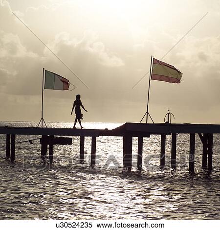 Stock Photography - Silhouette of Woman walking along Pier at Moorea in Tahiti. Fotosearch