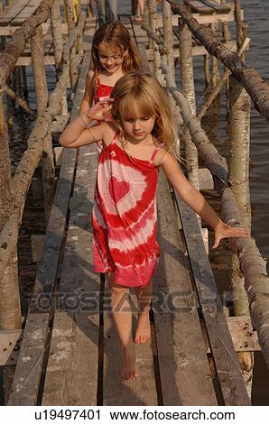 Two young girls walking on wooden pier View Large Photo Image Stock Image - Two young girls walking on wooden pier. Fotosearch