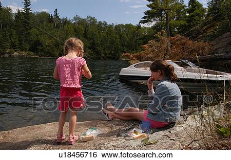 Stock Photograph - Rear view of a young girl and her mother on rock. Fotosearch