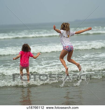 Two girls jumping in water on beach View Large Photo Image Stock Image - Two girls jumping in water on beach. Fotosearch