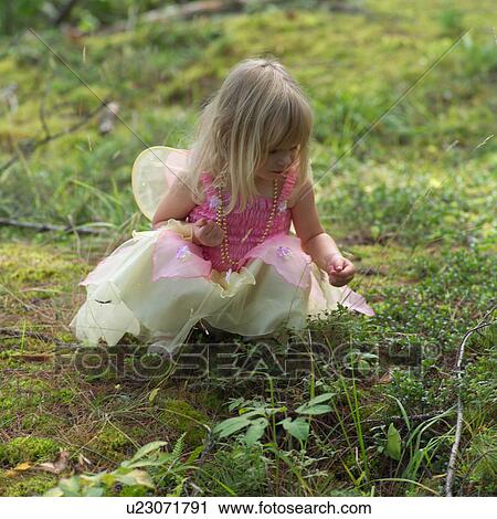 Stock Image - Young girl in a fairy costume squatting in the grass. Fotosearch