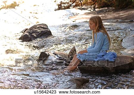 Stock Image - Girl sitting at edge of river. Fotosearch