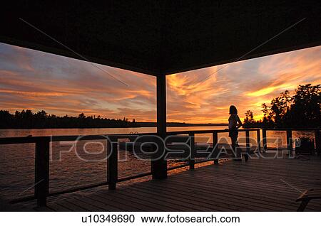 Stock Image - Silhouette of a deck with sunset over lake. Fotosearch