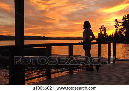 Stock Image - Silhouette of woman standing on a deck. Fotosearch