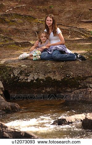 Stock Image - Two girls sitting at edge of river. Fotosearch