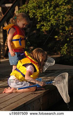 Stock Photo - Two girls with nets at edge of dock. Fotosearch