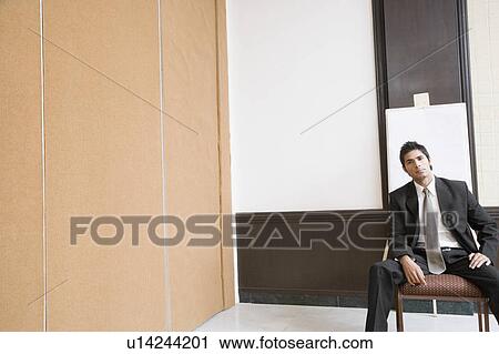 Businessman sitting in front of a whiteboard and looking serious View Large Photo Image Stock Image - Businessman sitting in front of a whiteboard and looking serious. Fotosearch