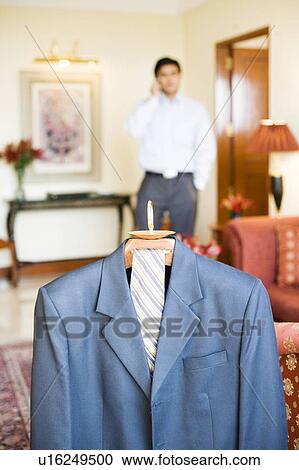 Stock Image - Close-up of a business suit hanging on a hanger with a businessman standing in the background. Fotosearch