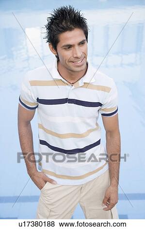 Close-up of a young man standing with his hand in his pocket and smiling View Large Photo Image Stock Photo - Close-up of a young man standing with his hand in his pocket and smiling. Fotosearch