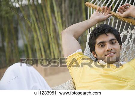 Stock Image - Portrait of a young man lying in a hammock and smiling. Fotosearch